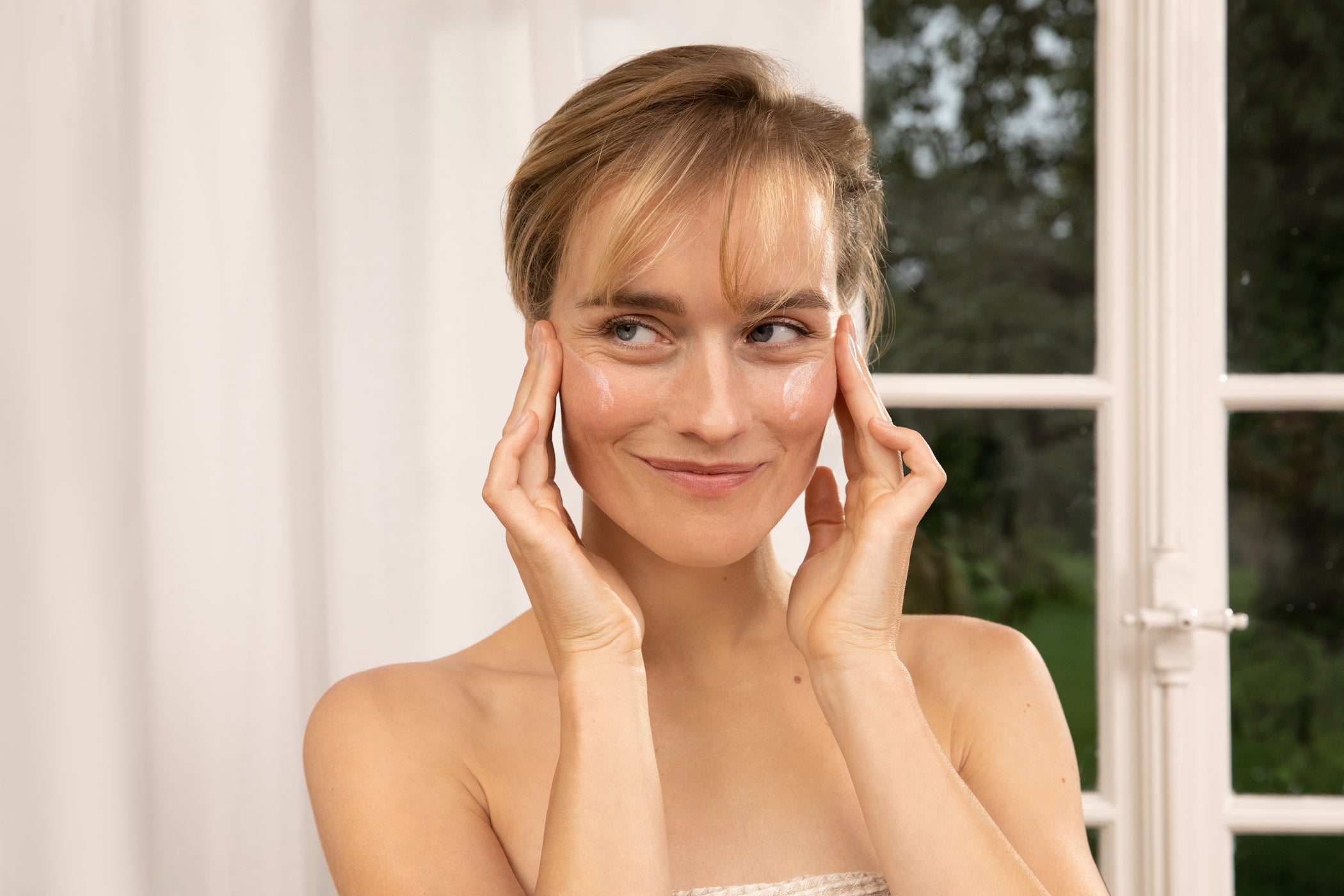 Femme blonde s'appliquant une protection solaire sur le visage