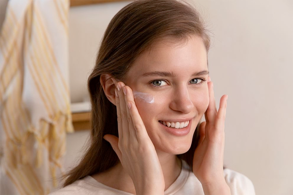 Femme étalant de la crème pour le visage sur les joues, souriant à la caméra