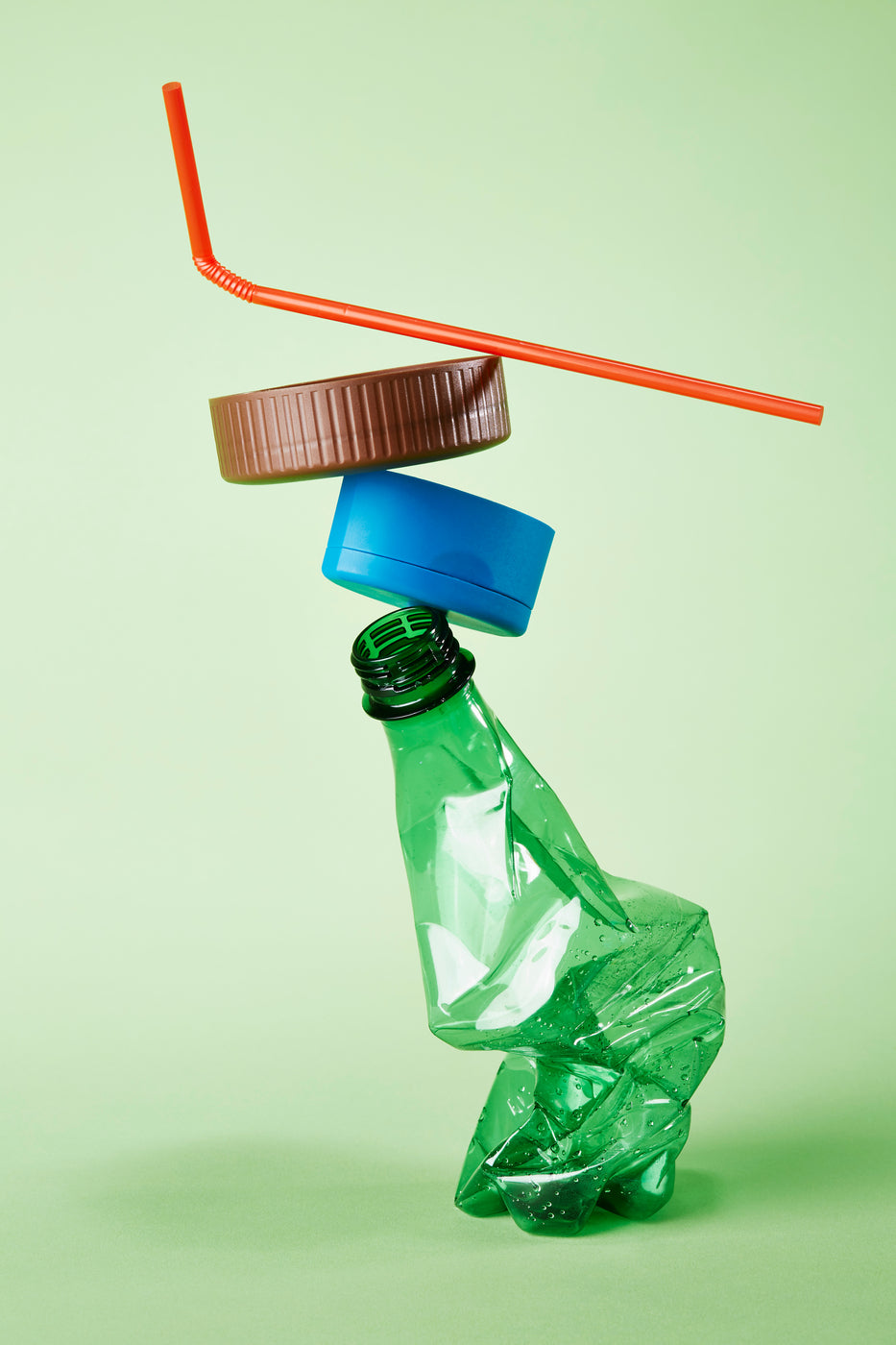 Leere Plastikflasche, Deckel und Strohhalm gestapelt vor grünem Hintergrund