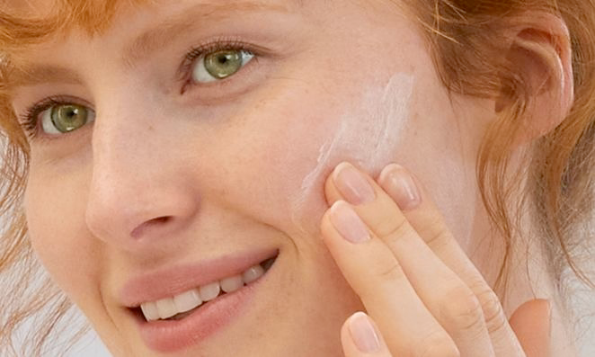 Femme rousse appliquant de la crème sur la joue, gros plan sur le soin de la peau