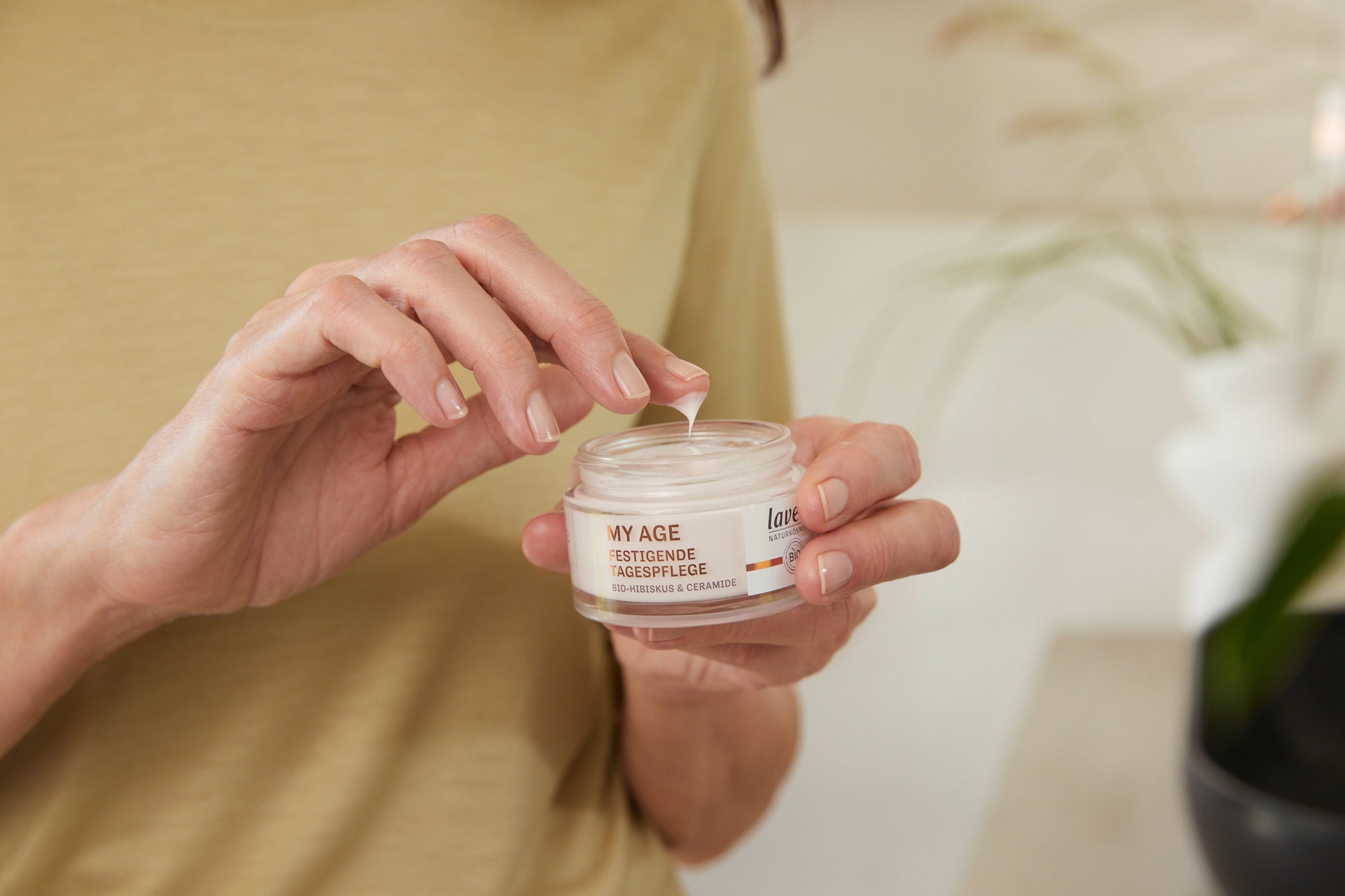 Frau hält My Age Tiegel mit der einen Hand und dippt mit der anderen Hand in die Creme