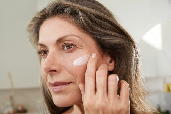 Reife Frau trägt weiße Gesichtscreme auf ihre Wange auf