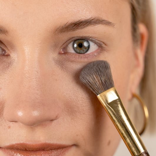 Pinceau de maquillage appliquant de la poudre sous l'œil, gros plan visage