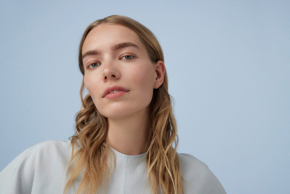 Portrait d'une jeune femme aux cheveux longs et fins sur fond bleu clair.