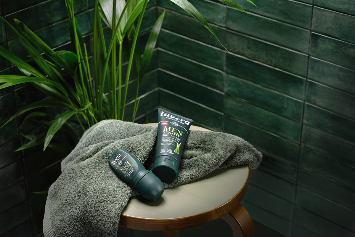 Men sensitive deo roll-on und Duschgel auf eiinem Hocker in einem grün gefliesten Badezimmer
