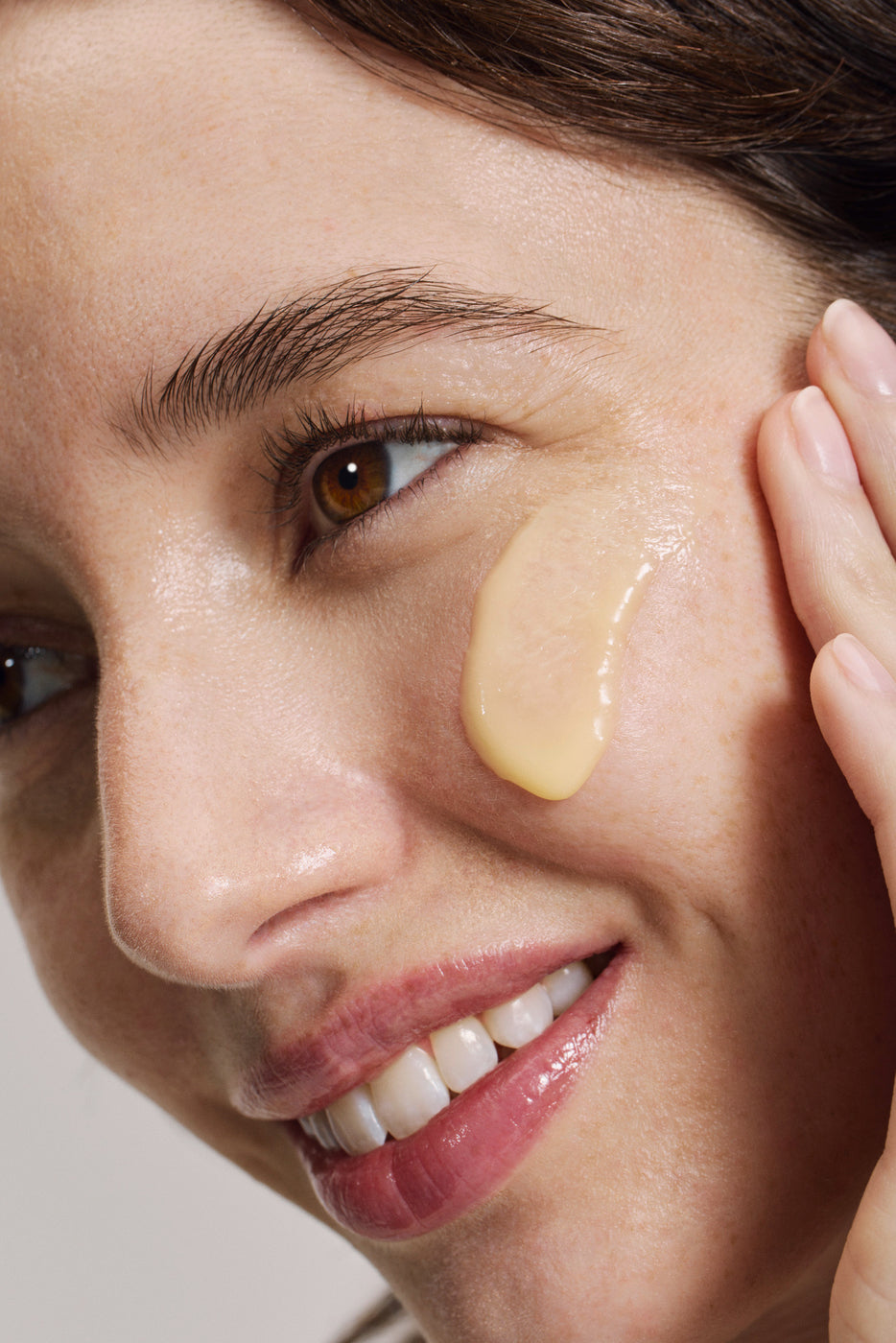 Gros plan d'une femme souriante avec crème dorée sous l'œil