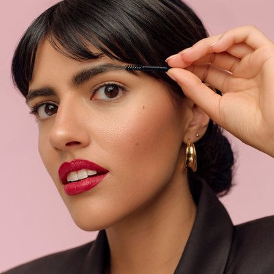 Femme brossant son sourcil avec une brosse sur fond rose