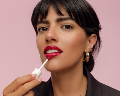 Femme appliquant un rouge à lèvres liquide rouge sur fond rose