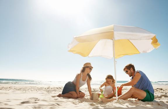 Famille avec enfant sous parasol à la plage en train de jouer dans le sable