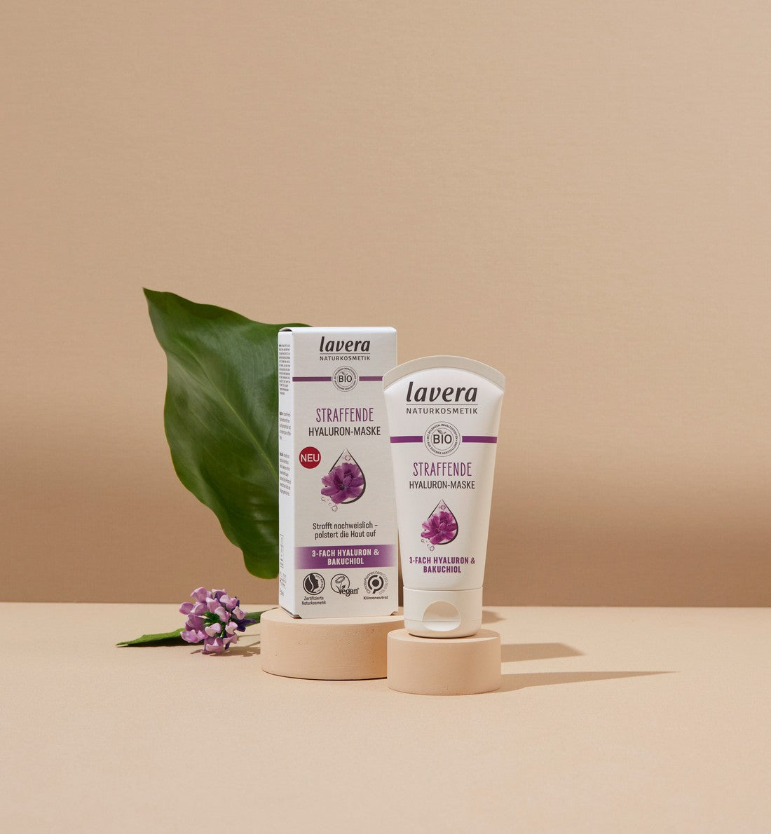 lavera Masque raffermissant à l'acide hyaluronique avec Bakuchiol, présenté de manière décorative sur fond beige avec éléments de feuilles