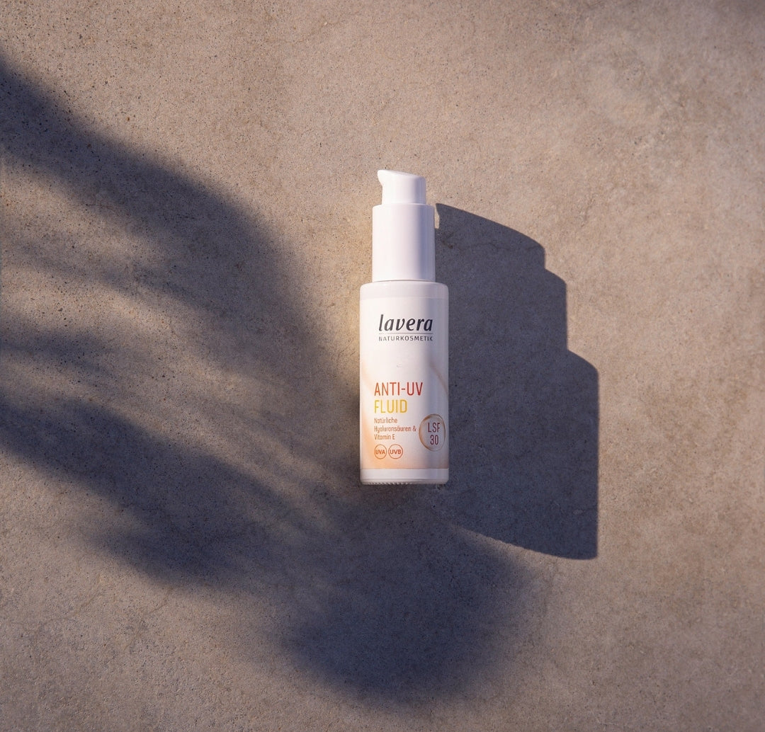 Eine Flasche lavera Anti-UV-Fluid liegt auf einer steinernen Oberfläche im Sonnenlicht und wirft einen langen Schatten.