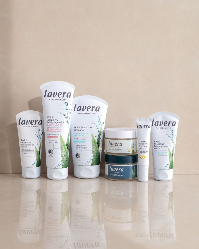Plusieurs produits de soin pour le visage lavera BASIS SENSITIVE sont disposés côte à côte sur une surface réfléchissante.