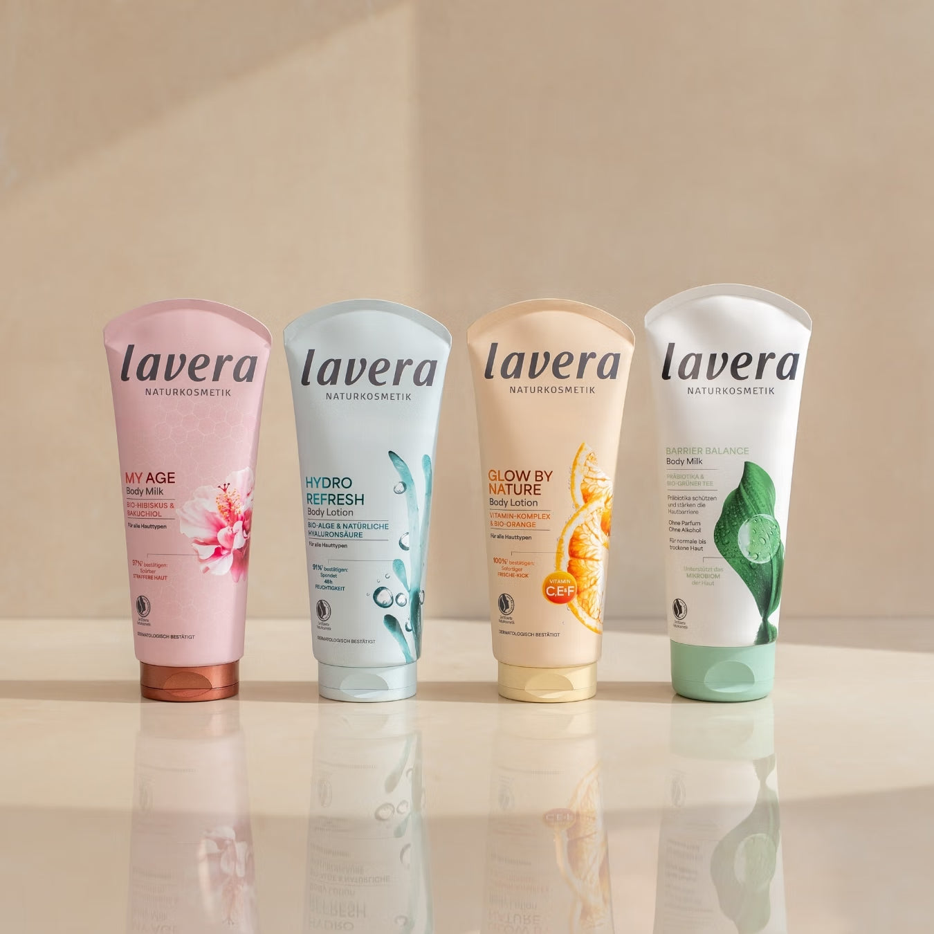 Vier lavera Körperlotionen stehen nebeneinander auf einer spiegelnden Oberfläche.