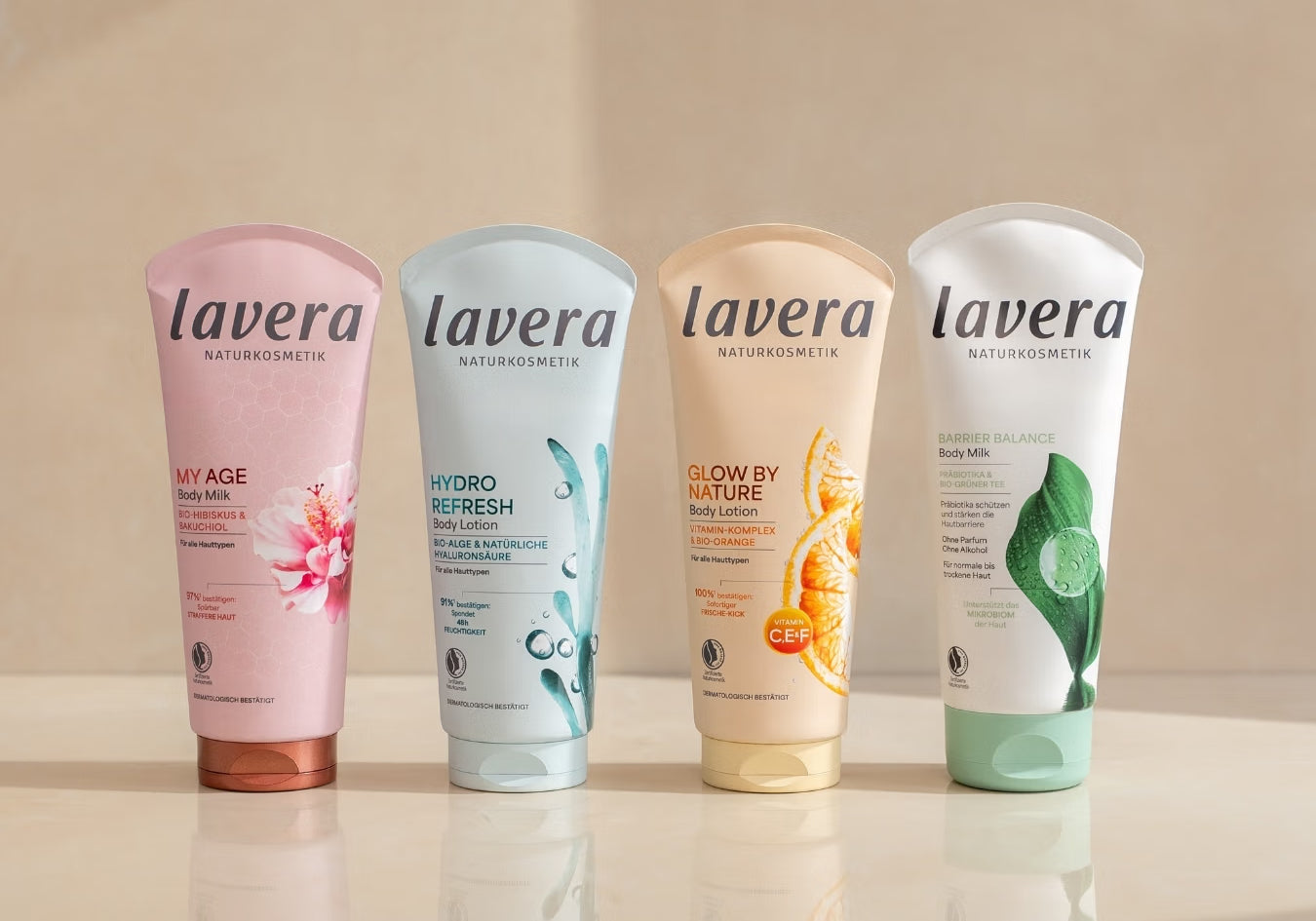 Vier lavera Körperlotionen stehen nebeneinander auf einer spiegelnden Oberfläche.