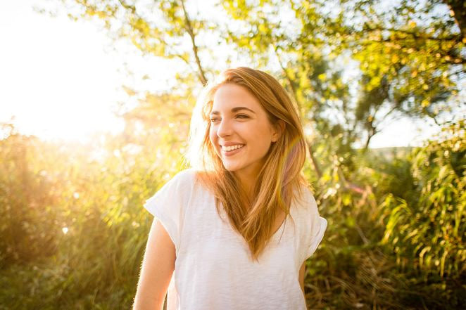 Femme dans un champ souriante à la lumière chaude du soleil