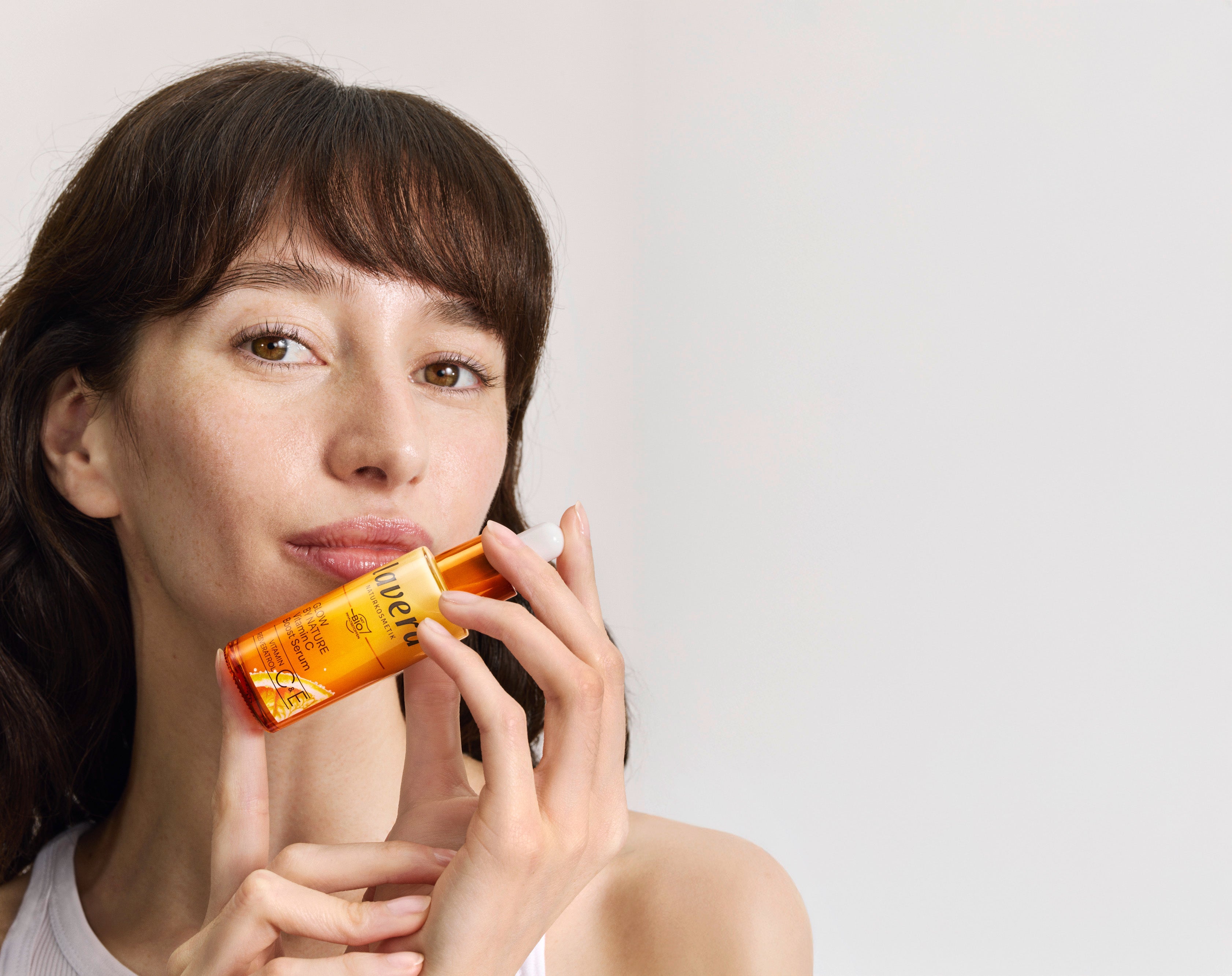 Eine Frau hält das lavera Glow by Nature Vitamin C Boost Serum in der Hand