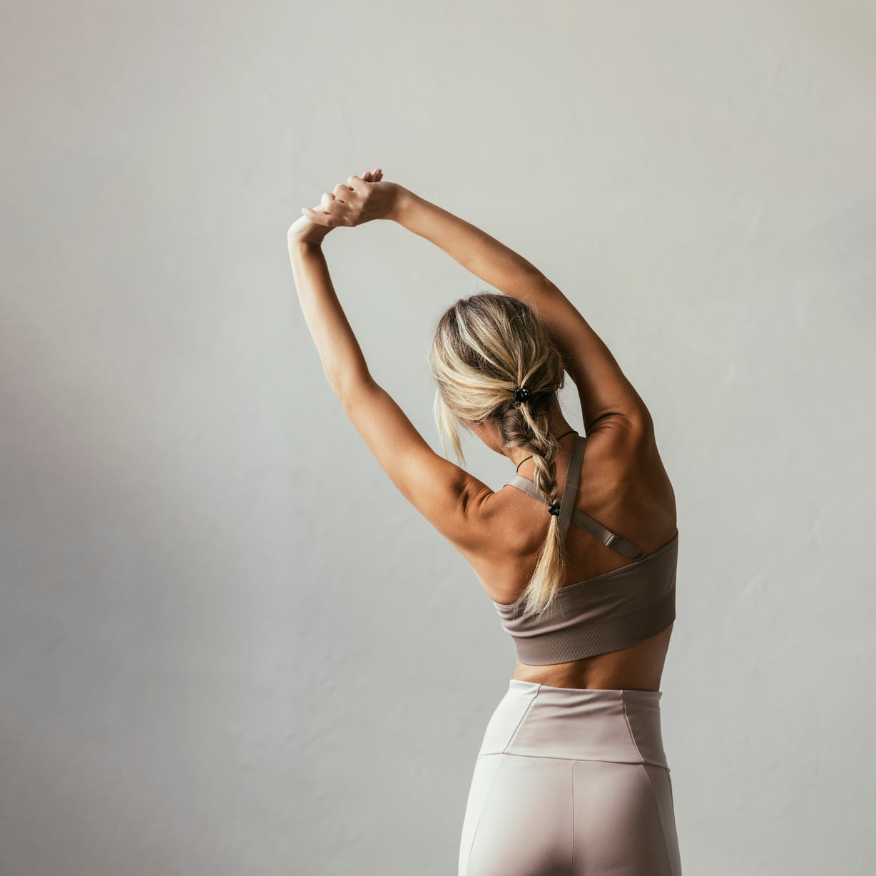 Femme en tenue de sport bras étirés au-dessus de la tête, vue de dos devant mur gris