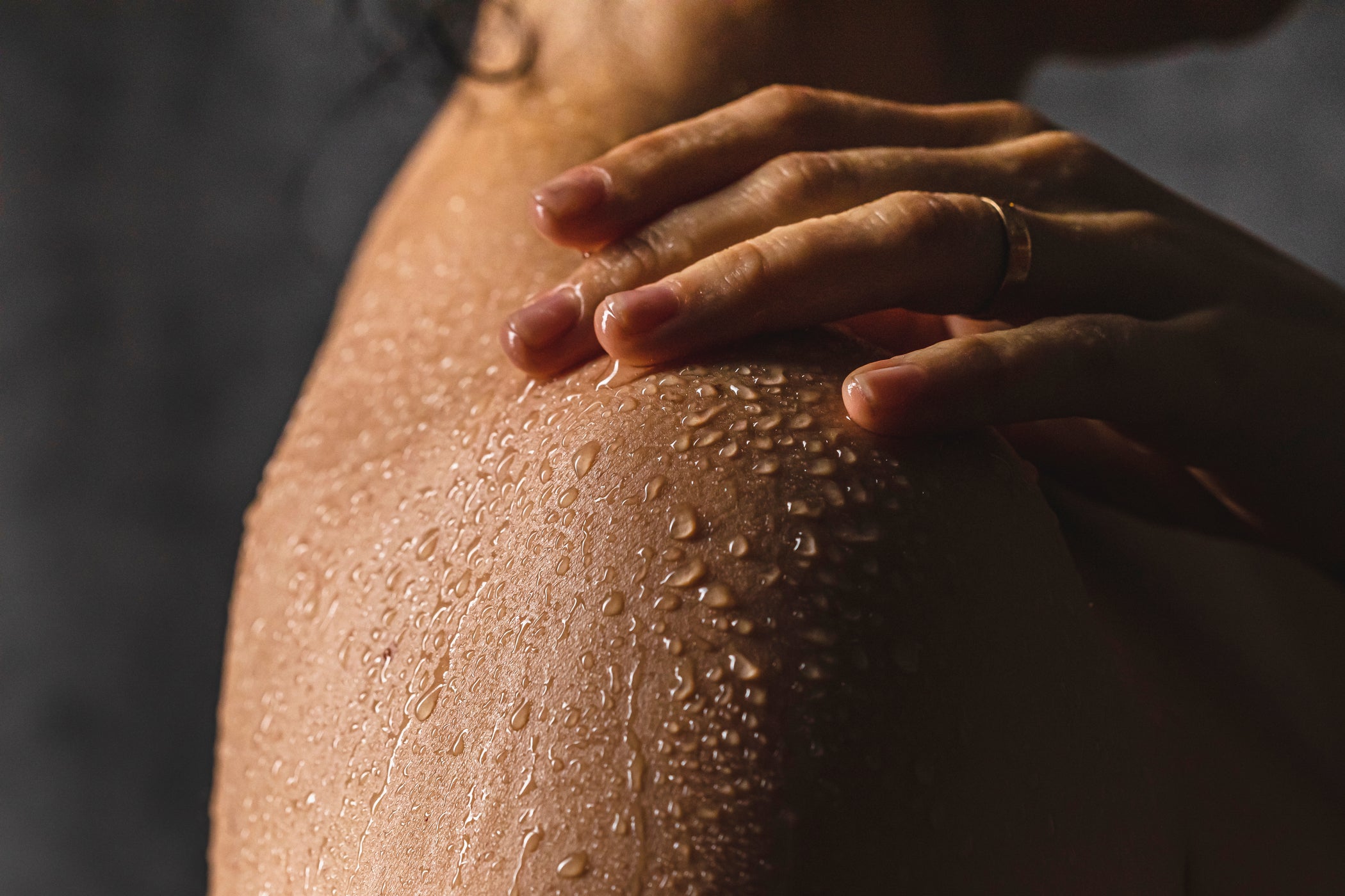 Gros plan de l'épaule d'une personne féminine couverte de gouttes d'eau – sur fond sombre