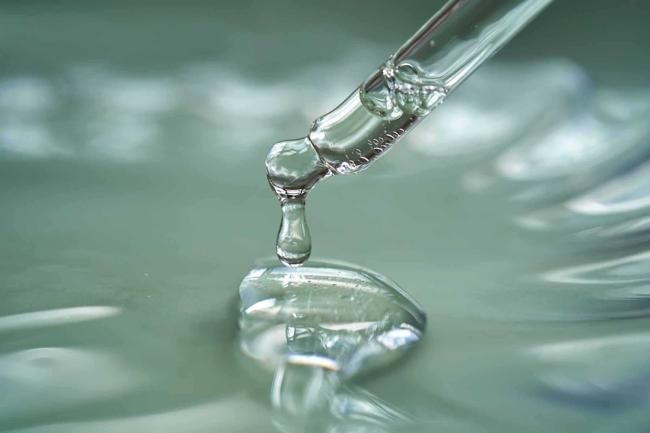 Pipette dépose du sérum transparent sur surface de gel brillante, macro