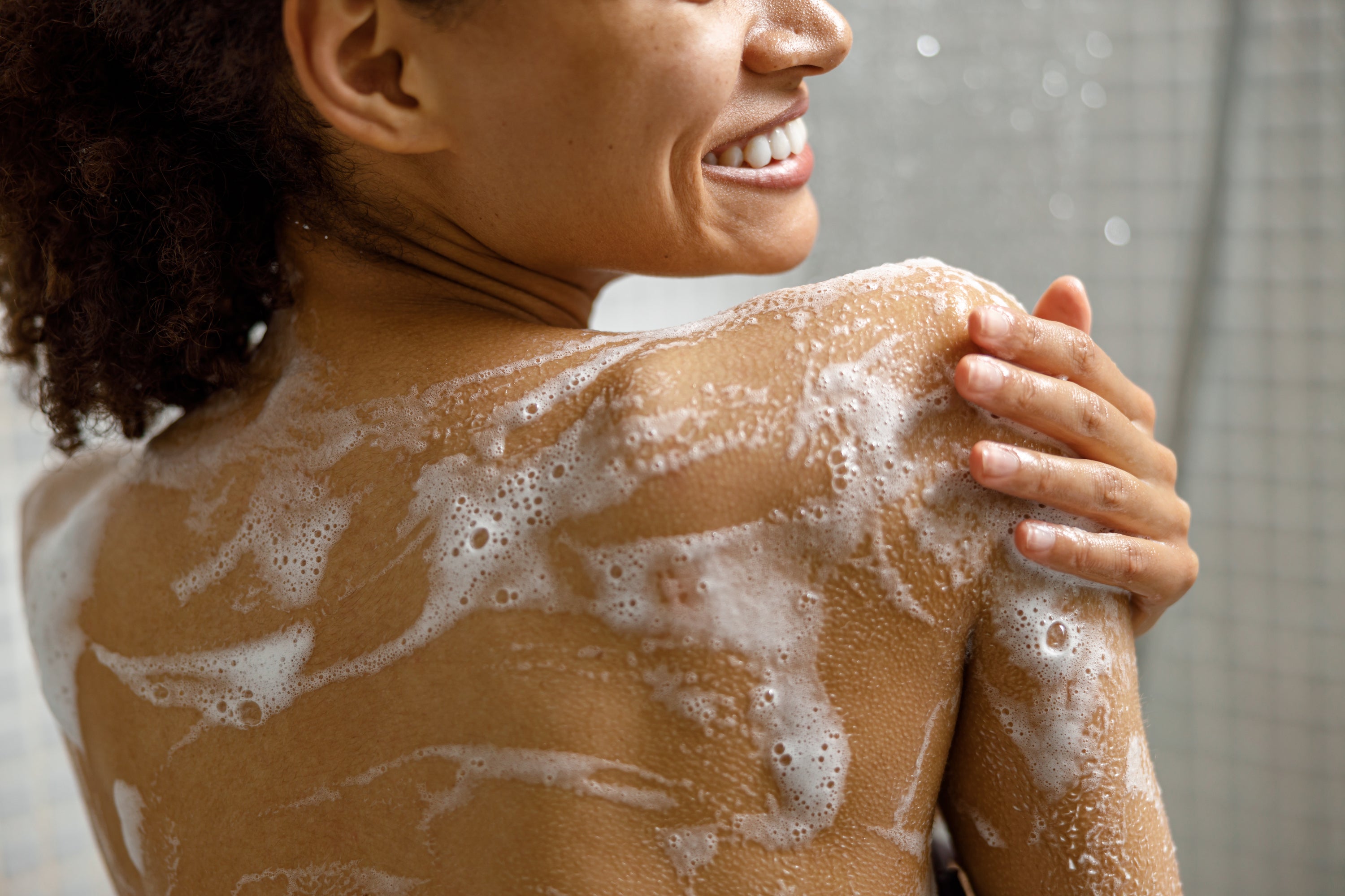 Gros plan du haut du dos d'une personne féminine sous la douche avec gel douche sur la peau