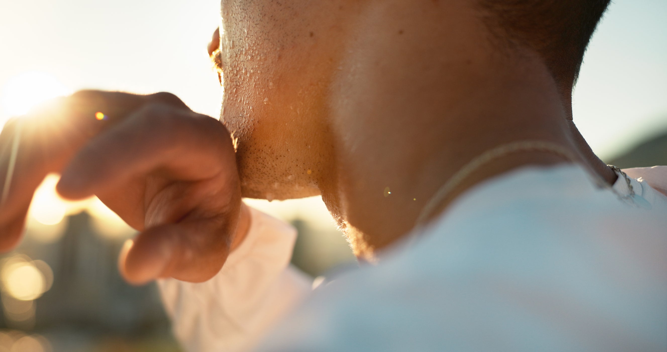 Homme essuyant la sueur du visage avec une serviette, lumière du soleil en arrière-plan