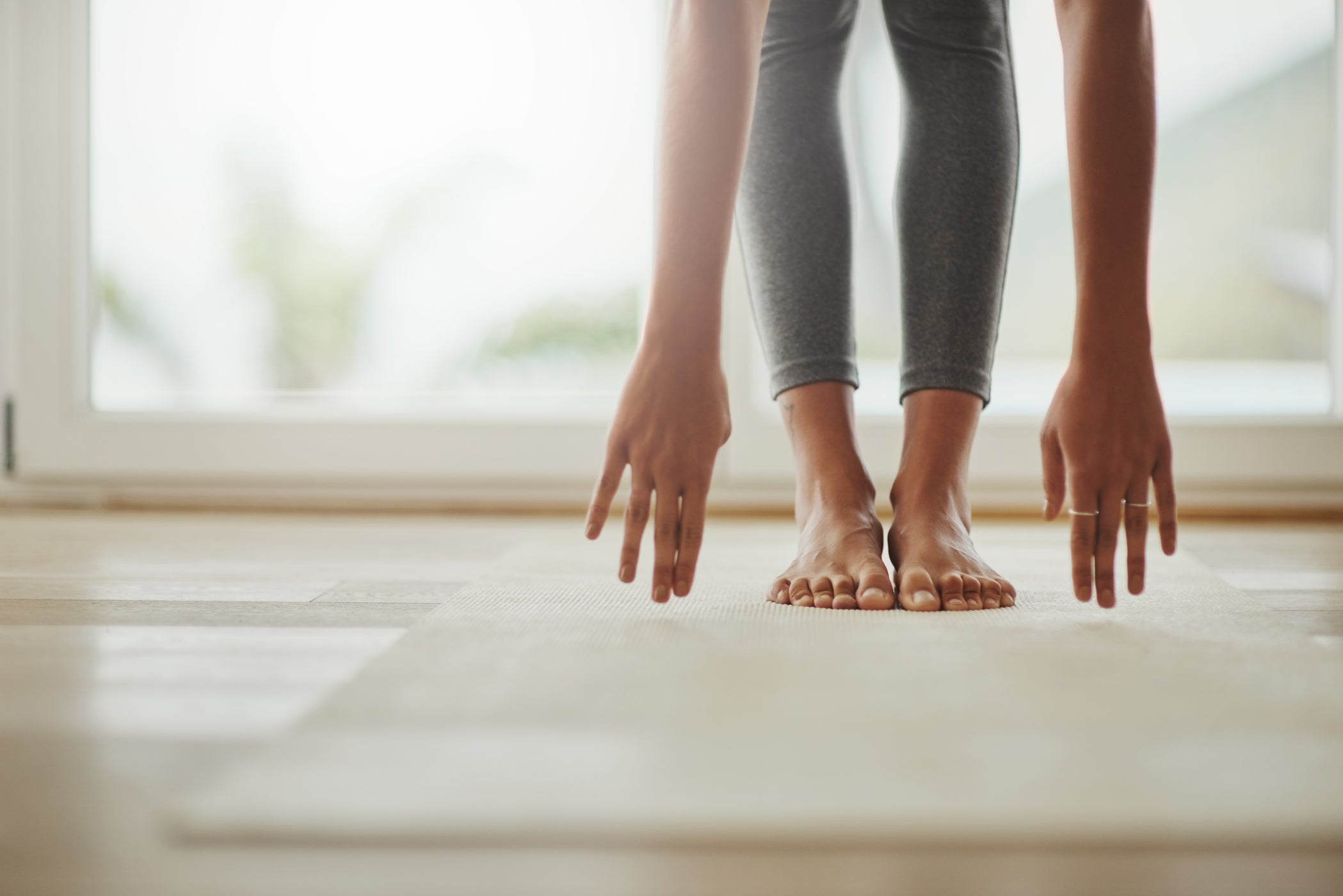 Partie inférieure des jambes et des bras d'une femme debout sur un tapis de yoga