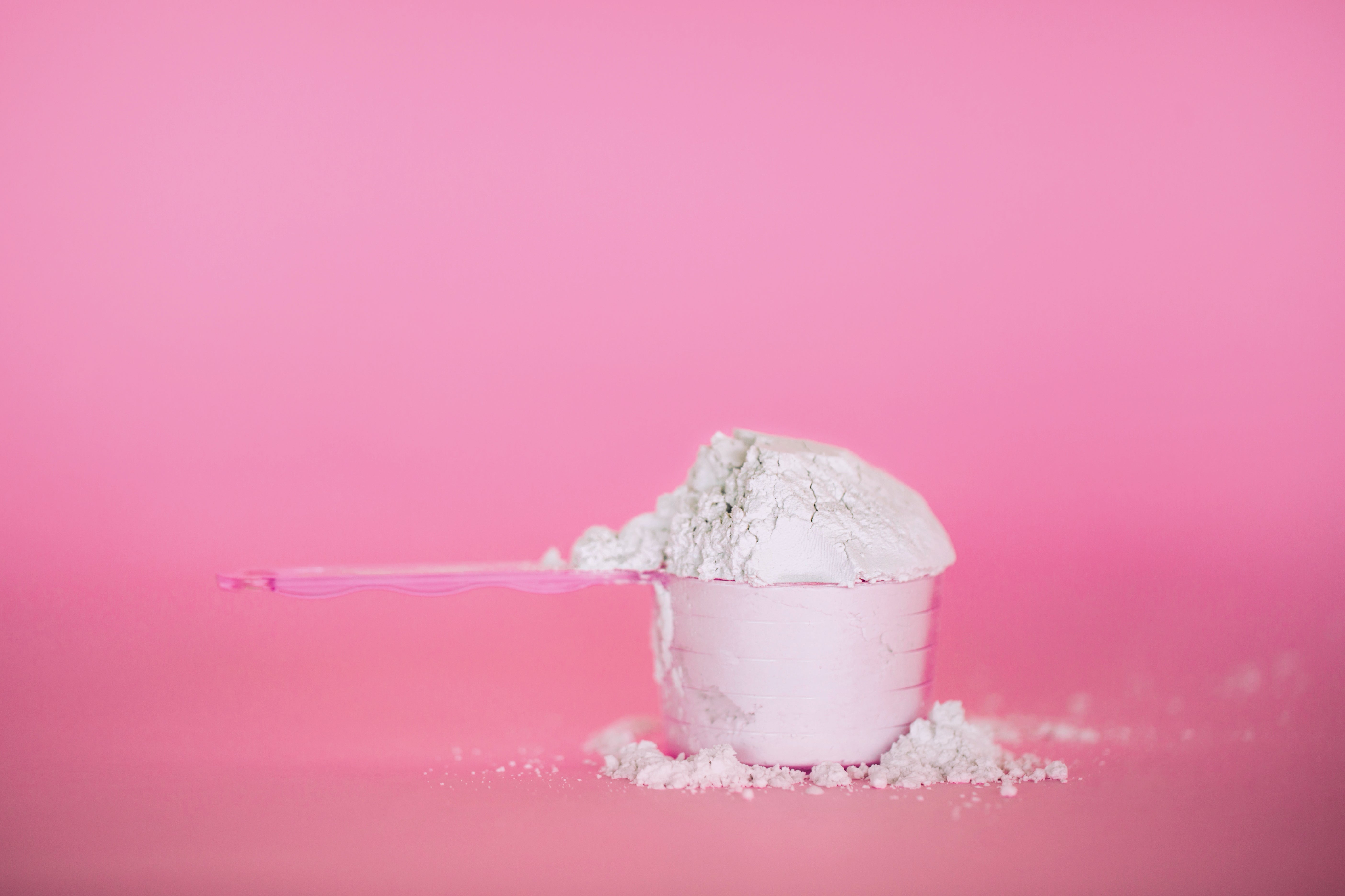 Messbecher mit weißem Pulver vor einem pinken Hintergrund