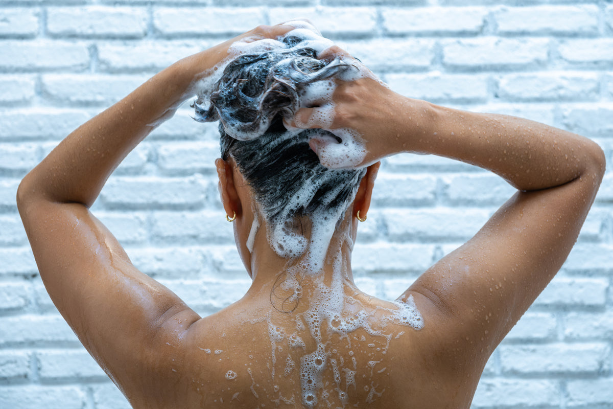 Weibliche Person steht mit dem Rücken zur Kamera und wäscht sich die Haare mit viel schaumigem Shampoo