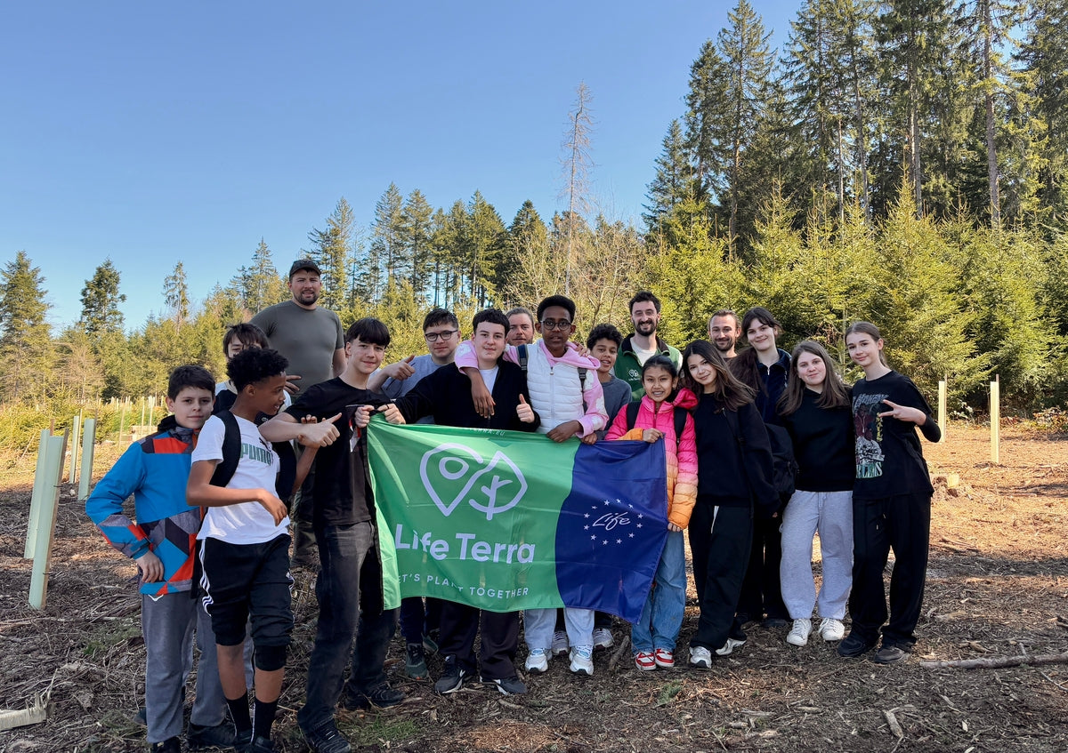 Gruppe aus Erwachsenen und Kindern im Wald mit einer LifeTerra Fahne in der Mitte