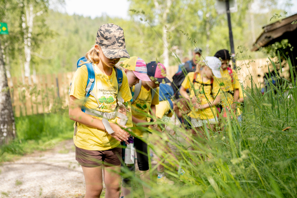 Kinder in gelben T-Shirts mit Kappies auf stehen draußen im Grünen