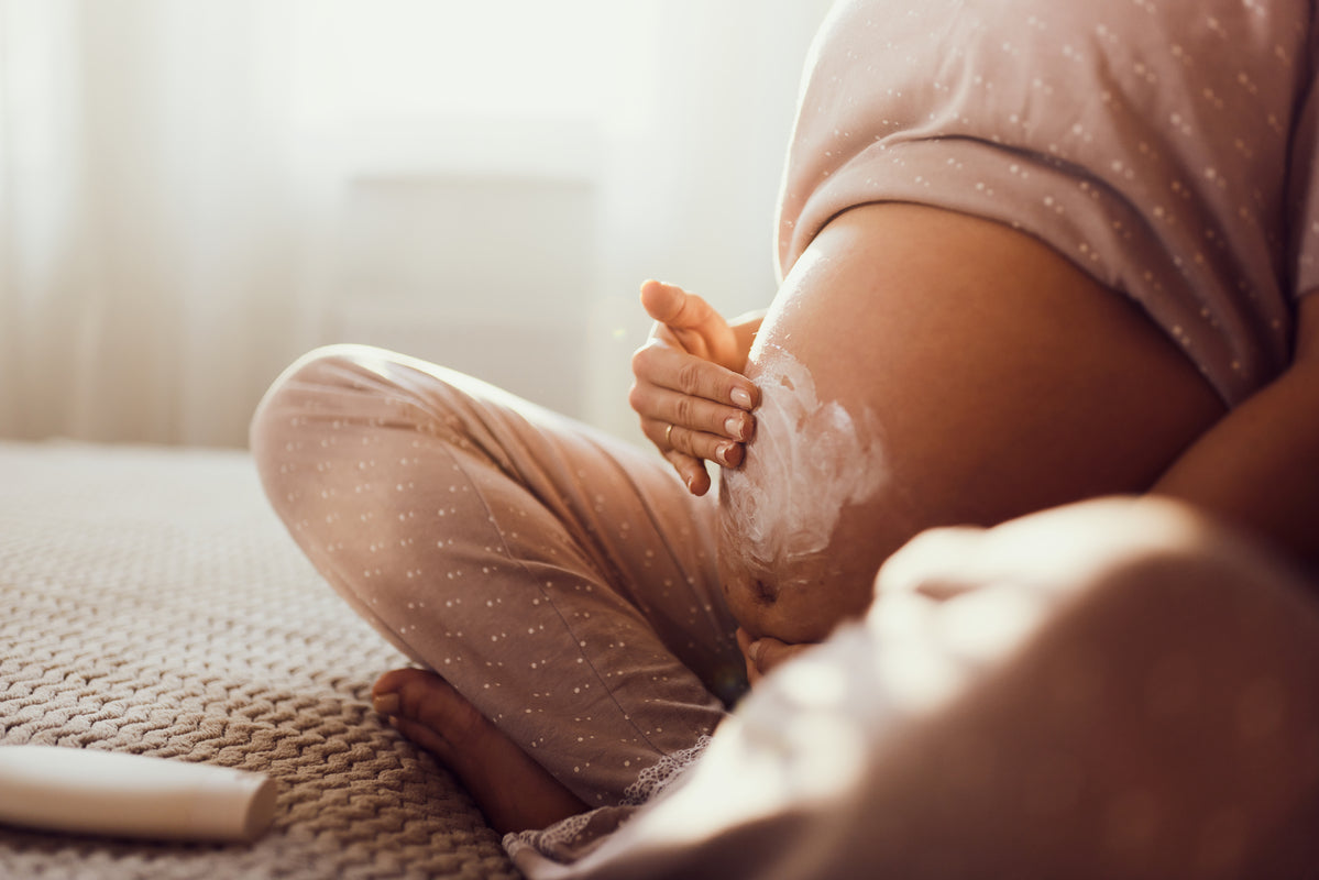 Femme enceinte en pyjama à pois appliquant de la crème sur son ventre