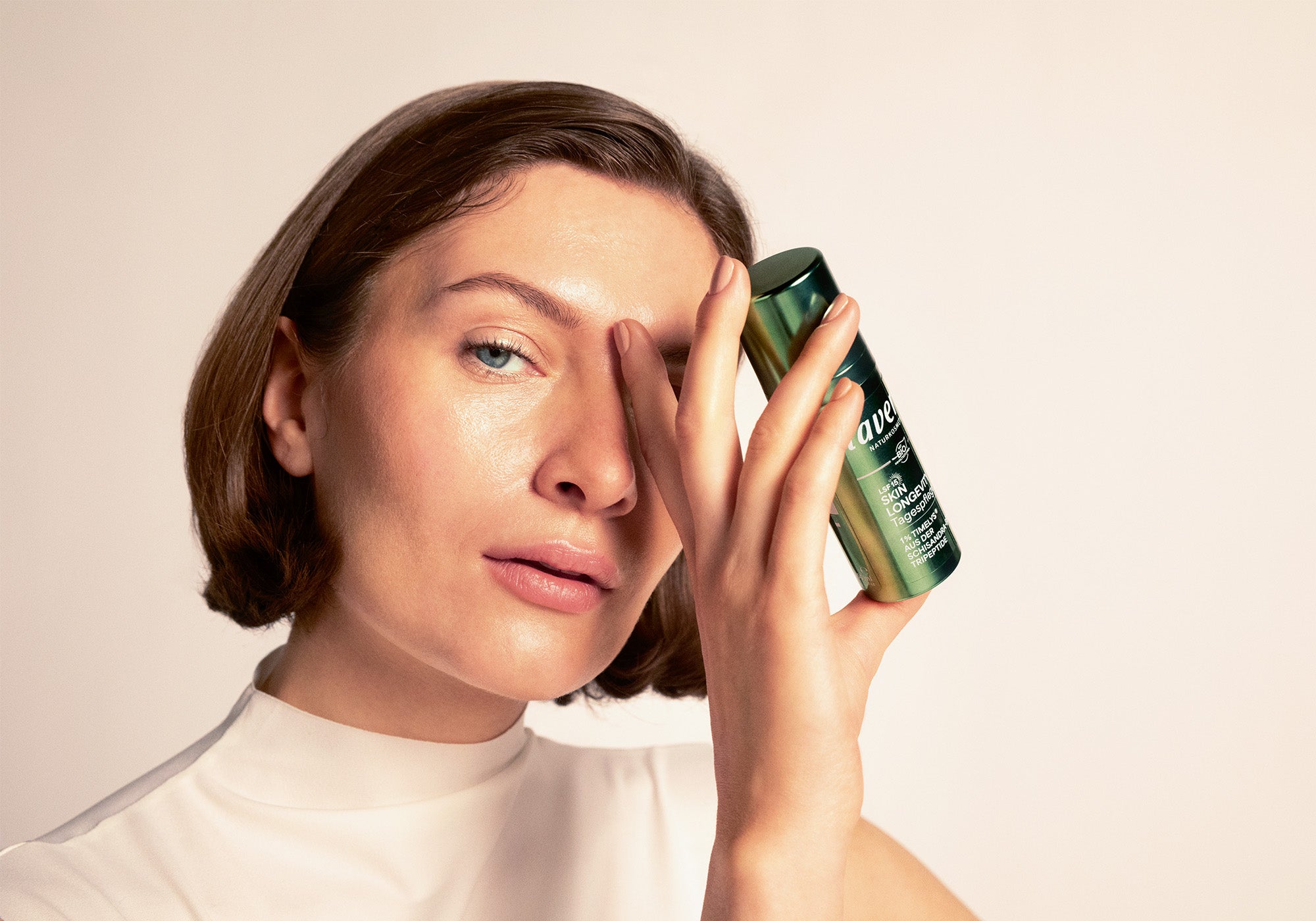 Frau mit schulterlangen dunkelblonden Haaren hält Skin Longevity Tagesflege in der Hand 