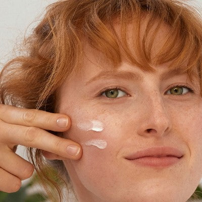 Femme rousse appliquant de la crème sur la joue, deux points visibles