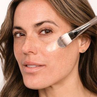 Femme applique fond de teint avec un pinceau sur la joue