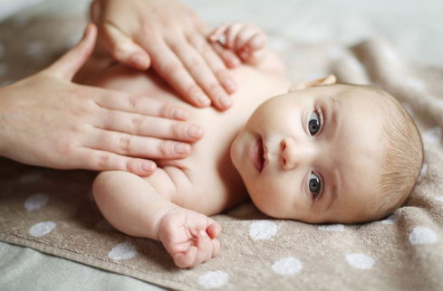 Bébé allongé sur couverture, mains massant doucement le torse, soin bébé
