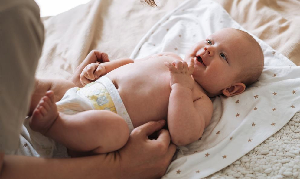 Bébé allongé sur couverture, mains massant le ventre et les jambes, soin bébé