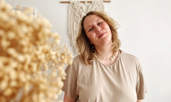 Femme sourit légèrement tête inclinée devant décoration macramé