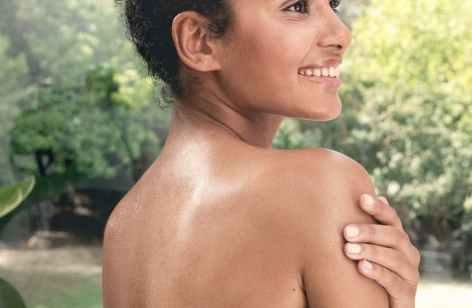 Femme en extérieur avec peau d'épaule brillante, main sur le bras, souriante