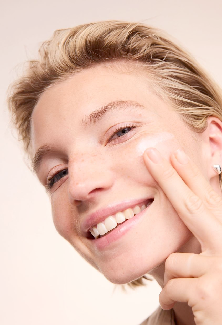 Gros plan : femme blonde masse crème visage sur la joue, souriante