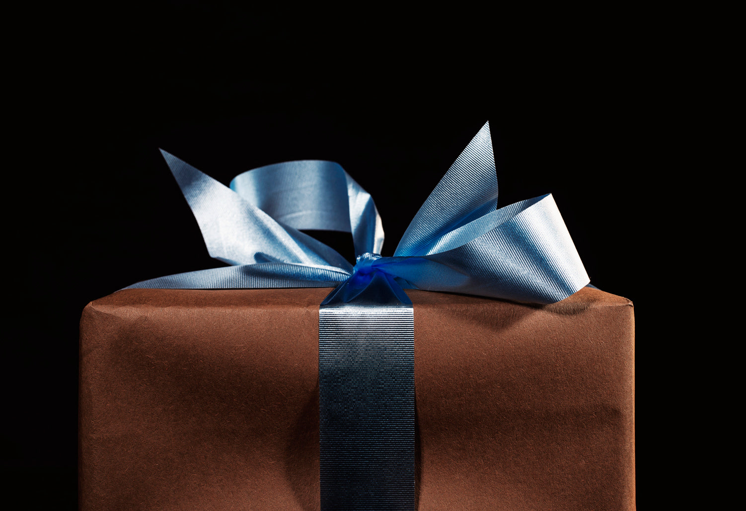 Cadeau en papier brun avec nœud bleu sur fond noir