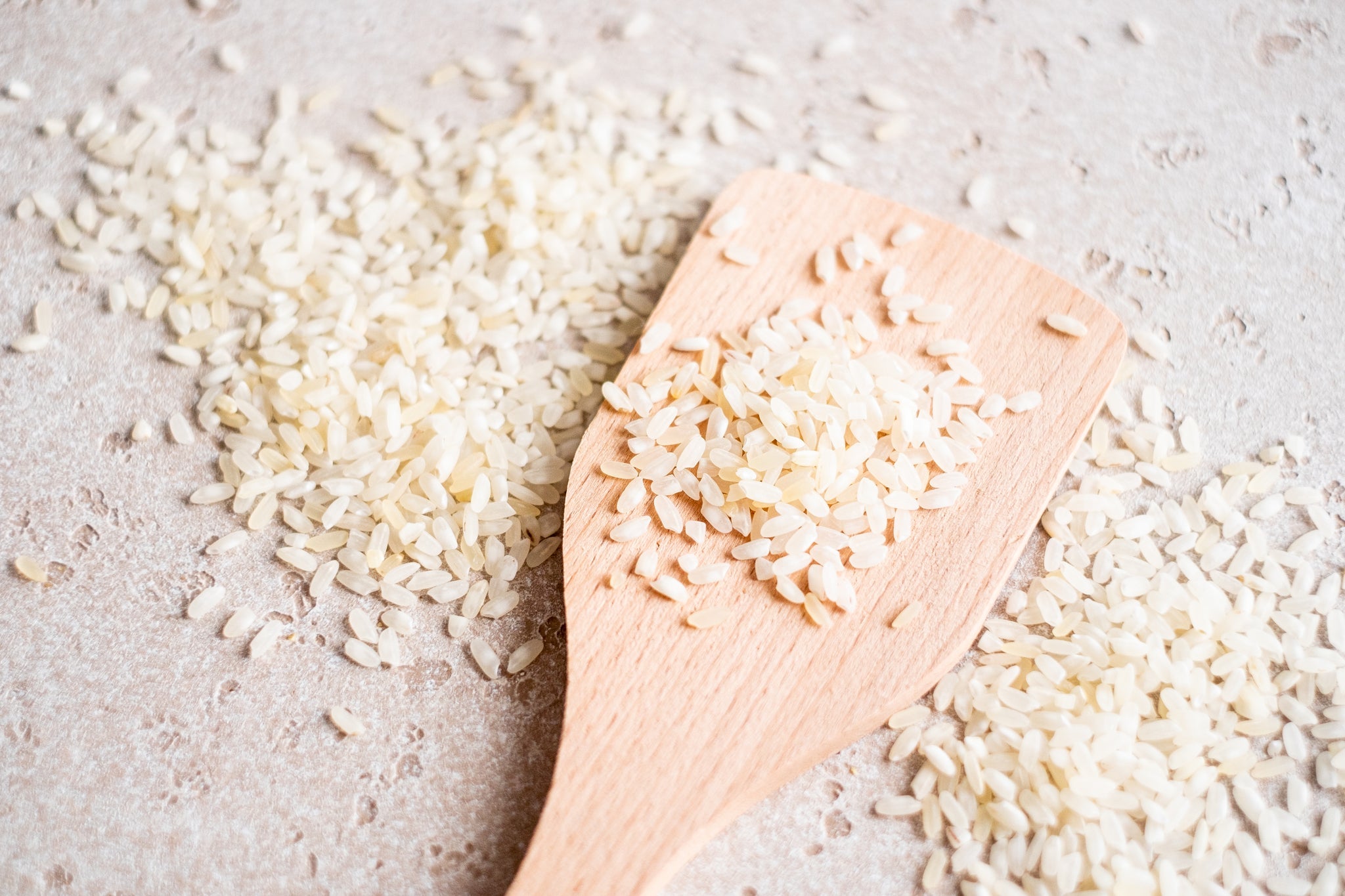 Holzlöffel mit weißen Reiskörnern, auf einem Tisch verstreut