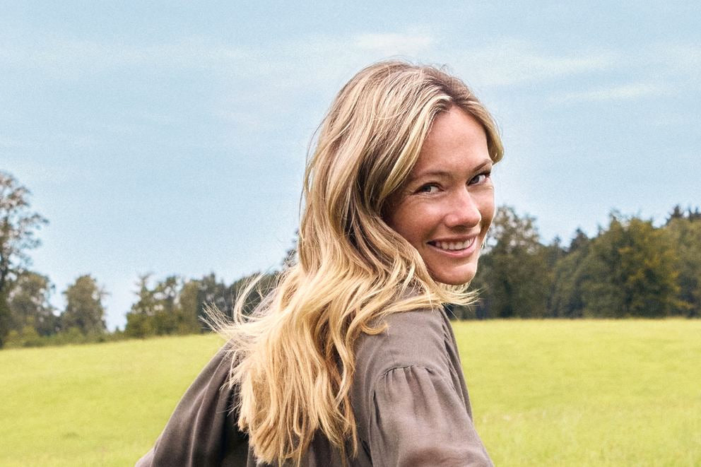 Femme blonde souriante regardant par-dessus l'épaule sur prairie verte, portrait extérieur