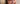Femme brune souriant à la caméra tout en appliquant de la crème sur son visage