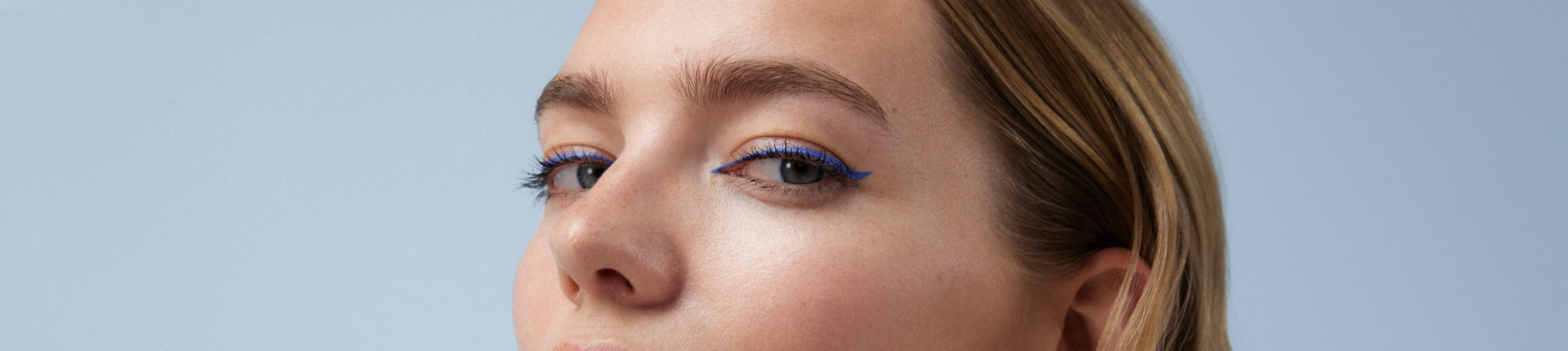 Femme aux cheveux blonds et maquillage moyennement prononcé en profil latéral regardant la caméra