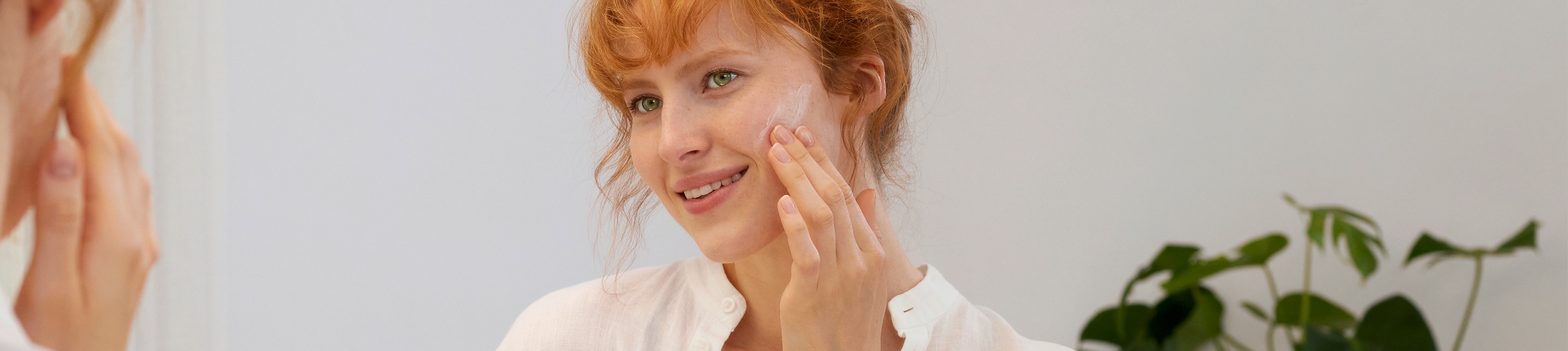 Gesichtspfege lavera Naturkosmetik Femme rousse se regarde dans le miroir et applique de la crème sur sa joue