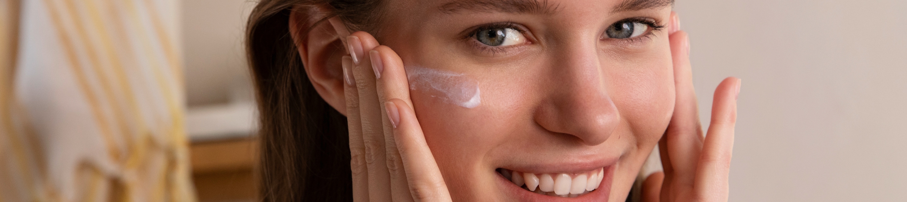 Gesichtsfluid lavera Naturkosmetik Femme brune souriant à la caméra tout en appliquant de la crème sur son visage