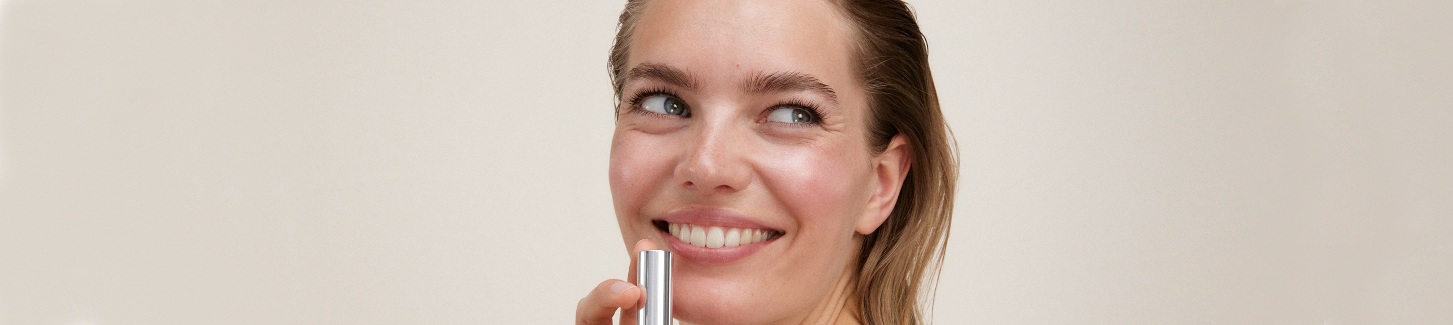 Femme blonde souriante regardant au-delà de la caméra tout en appliquant le rouge à lèvres lavera cosmétiques naturels sur ses lèvres