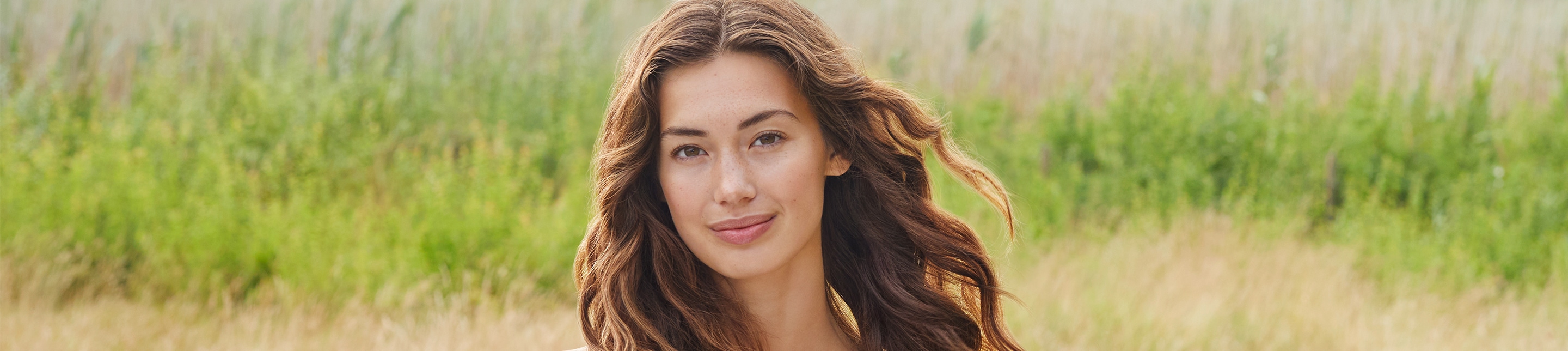 Haarpflege lavera Naturkosmetik Les cheveux d’une femme dansent au vent alors qu’elle se trouve en pleine nature, son visage baigné de lumière